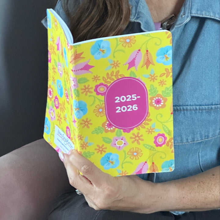 Person holding a colorful planner with floral design and '2025-2026' text.